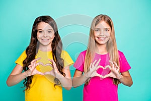 Photo of two nice good kind friendly girls long haired wearing yellow and pink t-shirts shaping hearts with their hands