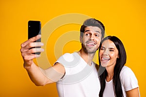 Photo of two people holding telephone taking selfies sticking tongues out of mouth playful mood wear casual clothes