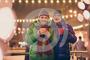 Photo of two people pensioner couple promenade hold cups drink hot chocolate smoke fly from mug wear mittens coat red