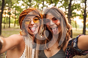 Photo of two stylish hippies women, smiling and taking selfie while walking in forest