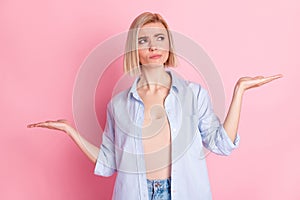 Photo of uncertain doubtful young woman look hold hands scales empty space choose product isolated on pink color