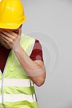 Photo of unhappy builder man in yellow helmet on empty gray background.