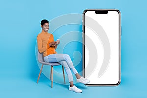 Photo of unisex person sit chair hold telephone poster empty space wear yellow shirt isolated blue color background photo