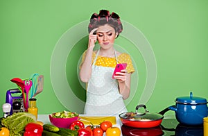 Photo of unsure girl prepare culinary dinner use smartphone watch video cant decide touch finger forehead wear yellow