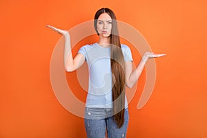 Photo of unsure long hairdo milennial lady hold empty space think wear blue t-shirt isolated on orange color background