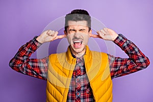 Photo of upset angry young man wear yellow sleeveless jacket fingers ears not want hear isolated violet color background