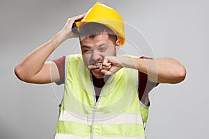 Photo of upset builder in yellow helmet in vest on empty gray background.