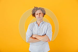 Photo of upset serious man 20s with curly hair standing with arm