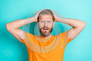 Photo of upset unhappy stressful man with blond hairstyle dressed orange t-shirt arms on head staring isolated on teal