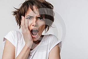 Photo of upset woman with short brown hair in basic t-shirt keeping hand over her face and screaming at camera