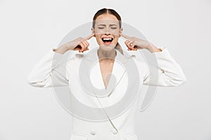 Photo of uptight nervous businesswoman 20s wearing elegant jacket screaming and plugging ears with fingers