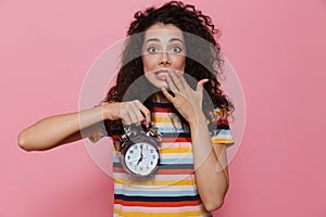 Photo of uptight woman 20s with curly hair holding alarm clock,