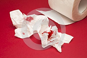 A photo of used of bloody toilet paper and a toilet paper roll on the red background. Menstrual, hemorrhoids bleeding. Blood