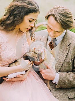 The photo of the vintage dressed just married holding the brown and white ferret and enjoying the down time in the green