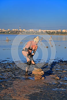 A woman in a bathing suit coats herself with healing mud from the estuary