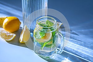 A photo of water with sliced â€‹â€‹lemon and mint leaves in a glass mug and chopped lemon slices next to a decanter