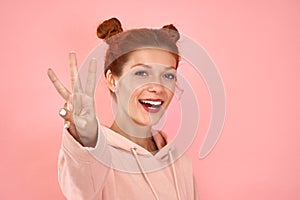 Photo of wavy curly charming Caucasian young redhead woman smiling toothily showing you three fingers isolated over pink