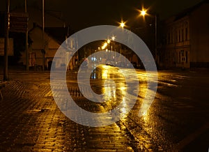 Wet empty street at night illuminated by street lamps