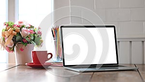 Photo of white blank screen computer laptop putting on working desk with bunch of flowers, notebook and pencil holder.