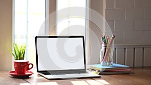 Photo of white blank screen computer laptop putting on working desk with bunch of flowers, notebook and pencil holder.