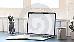 Photo of white blank screen laptop putting on the modern working desk including potted plant, coffee cup, notebook and pencil