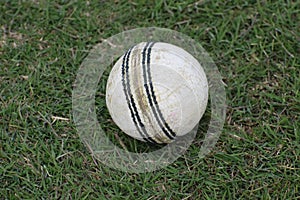 Photo of a white leather cricket ball with stitched seams on grass, cricket ball on green grass pitch with copy space, Close up