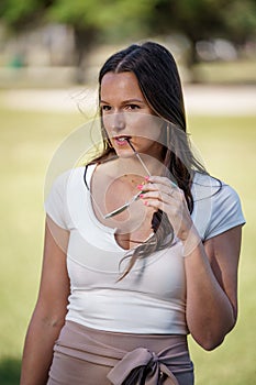 Photo of a woman glancing away from camera with sunglasses leg in her mouth