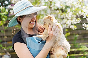 Photo of woman in hat holding ginger cat in garden