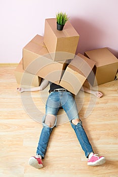 Photo of woman in jeans lying under cardboard boxes