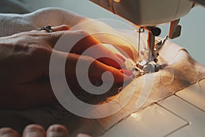 Photo of woman`s hands in process of sewing linen dress using automatic sewing machine photo