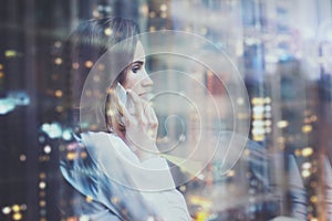 Photo woman wearing white shirt, talking smartphone and holding business plans in hands. Open space loft office. Panoramic windows