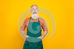 Photo of wondered senior man dream look empty space minded employment shopkeeper isolated over yellow color background