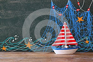 Photo of wooden sailing boat in front of chalkboard with nautical illustrations.