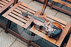 Photo of wooden violin on chairs. Horizontal shot. Live music on special occasion. Outdoor photo. Musical instrument under open
