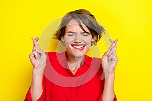 Photo of worried girl closed eyes biting lips crossed fingers isolated on yellow color background