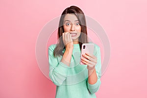 Photo of worried girl hold telephone gnaw bite fingernails look camera wear turquoise sweater isolated pink color