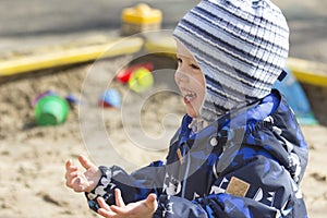 A smiling 2-year- old boy playing in a sandbox