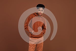 Photo of young african handsome guy hands in pocket wear sweatshirt serious isolated over brown color background