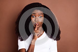Photo of young afro girl cover lips fingers shh shut up keep secret conspiracy isolated over brown color background