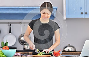 Photo of young asian woman smiling while cooking salad with fresh vegetables in kitchen interior at home