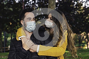 Photo of a young and attractive couple on a date in the park wearing a face mask and hugging