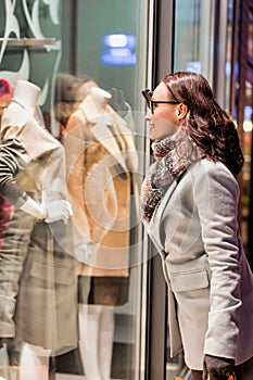 Portrait of young attractive woman looking at the dress on a manequin in shop through the window photo