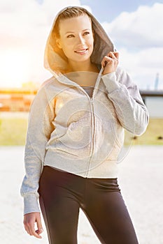 Portrait of young attractive woman smiling while standing and zipping her jacket in park photo