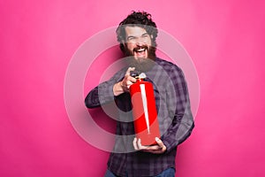 Photo of young bearded man in shirt holding fire extinguisher over pink background