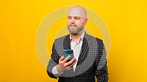 Photo of young bearded man in suit holding smartphone and lookinh away at copyspace