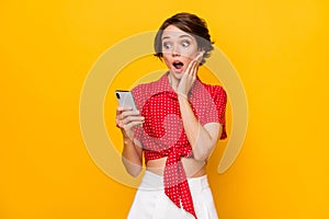 Photo of young beautiful amazed shocked surprised girl see unexpected news in cellphone  on yellow color