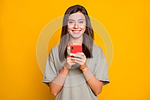 Photo of young beautiful happy positive cheerful smiling girl typing in smartphone isolated on yellow color background