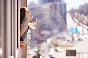 Photo of young beautiful happy smiling woman with long hair near the window. Sunny day. City lifestyle.