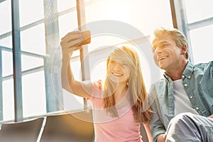 Portrait of young beautiful teenage girl taking selfie with her father in airport