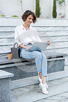Young beautiful woman sitting outdoors using laptop computer